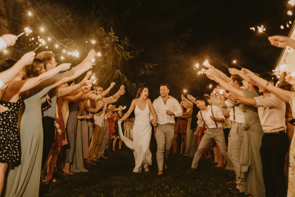 Newlywed couple celebrating with guests holding sparklers at night — joyful wedding moment filled with love and connection